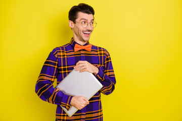 Photo of young excited man happy positive smile look empty space hold laptop isolated over yellow color background