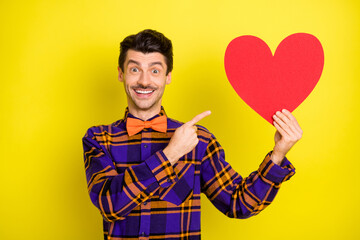 Photo of happy smiling cheerful positive man point finger at big red paper heart valentine day isolated on yellow color background