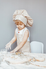 Portrait of a little cook kneading dough in an apron and a chef's hat.