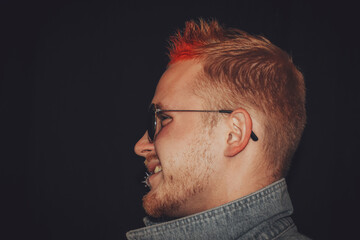 Profile portrait of handsome young male punk with Iroquois haircut, piercing and red hair isolated on black background