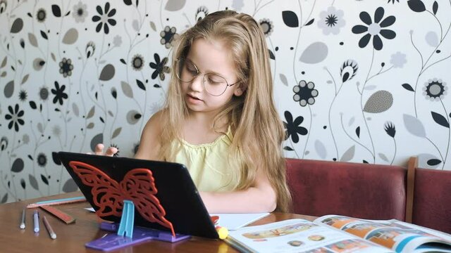 Distance learning. Home online learning. Little girl teaches English, speaks with a teacher online.