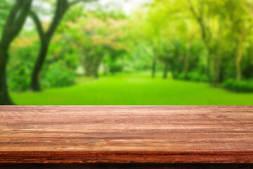 Wooden table with Blurry image of green grass meadow field and green trees in background.