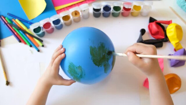 Child making planet for earth day from balloon. drawing blue ball with green continents. Protection of environment, Save our planet. Ecology concept. art learning and education love earth save world