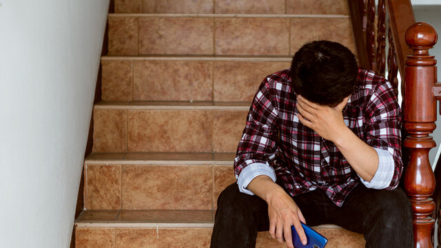 A young man sits anxious at the stairs because of losing his job during the coronavirus outbreak.