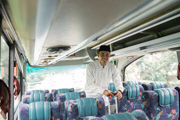 happy asian muslim man doing eid mubarak traveling back to his hometown by riding a bus