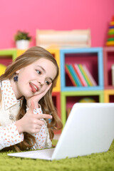 Emotional cute girl using laptop while lying on floor