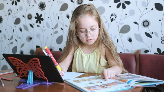 Distance learning. Home online learning. Little girl teaches English, speaks with a teacher online.