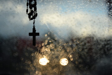 Rosary, cross, wet window and lights of an oncoming car