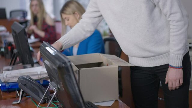 Unrecognizable man packing cardboard box in office with blurred women working at background. Unknown male Caucasian employee being fired indoors. Unemployment and stress