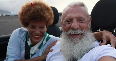 Trendy senior couple having fun inside convertible car in summer vacation - Joyful elderly people taking selfie on cabriolet car - Powered by Adobe