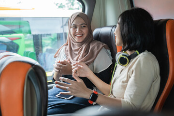 two young women chatting with hand gesture against the window background while sitting on the bus