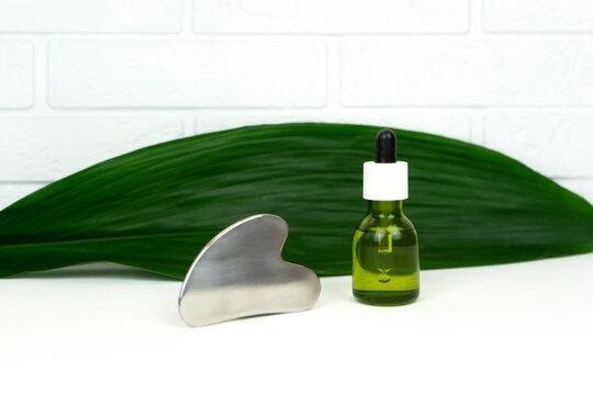 An unbranded green CBD cannabis oil with a Gua sha massaging scraping tool lie on a green leaf.