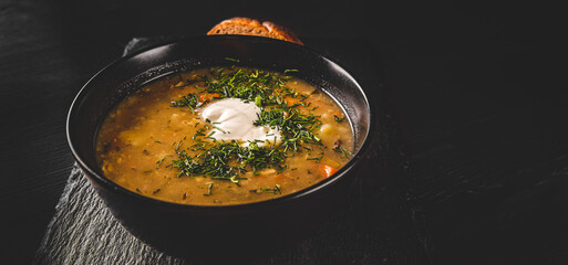 Soup with pickled cucumbers and pearl barley in black bowl on black wooden table background