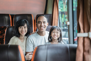Asian mom and dad smile at the camera while cradling their daughter while sitting on the bus seat during the trip