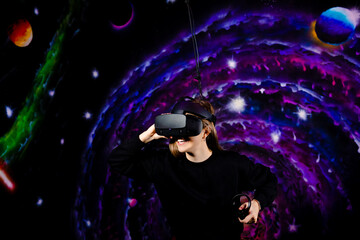 A young girl actively plays video games wearing VR virtual reality glasses. Space background, stars and planets.