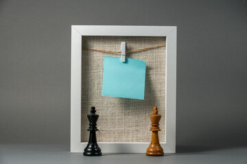 White frame with hanging chit on the clip and the cord and linen bacground and kings of chess.