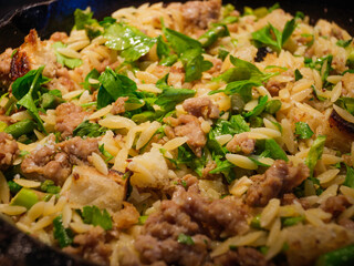 Cooking Orzo Meal in a Black Cast Iron Skillet. One-Pot Skillet Dinner with Sausage, Asparagus, Orzo, and Bread Crumbs.