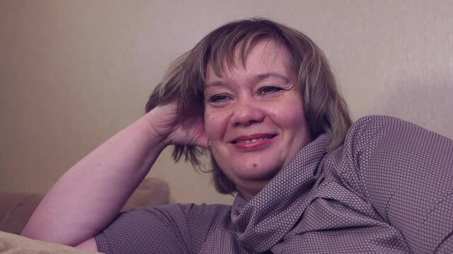 Happy woman is lying on the couch, watching tv movie and smiling. The female watches TV dreams of breathing fresh air, on a comfortable sofa in the living room, a stress-free cozy day at home.