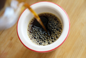 Pouring freshly brewed black pour over filter coffee into cup close-up.