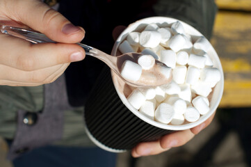 Child's hands with paper cup of cocoa with marshmallows on street