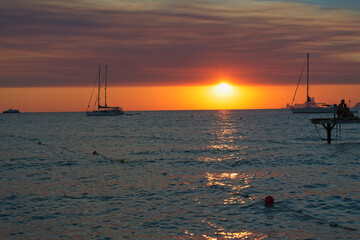 A beautiful sunset over the sea on the island of Formentera in Spain, with silhouettes of anchored sailboats and the sun on the horizon