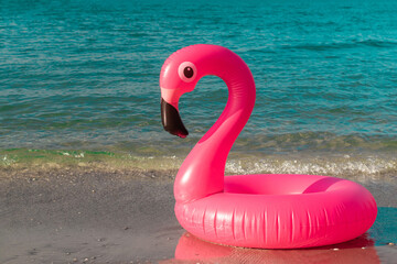 Summer concept background. Pink inflatable flamingo in blue ocean water for sea summer beach...