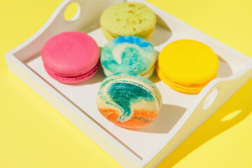 Assortment of colorful macaroons on white wooden tray on yellow background with sunlit. Dessert concept.