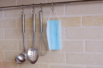 Kitchen appliances hang on hooks against a white brick wall, and a medical mask hangs among them.