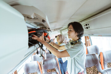 a young man in headphones puts a bag on a shelf while standing on the bus