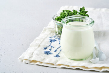 Sour cream or natural yogurt in a glass jar with spoons, health and diet concept on light gray...