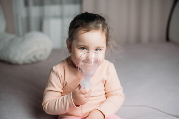 little cute girl sitting on the bed in the bedroom doing inhalation by herself