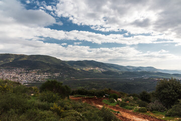 Naklejka premium A view of a mountain range and a green valley in the morning at sunrise, against a dramatic backdrop of blue skies and clouds. North District Israel. High quality photo. Travel concept hiking