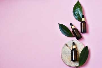 Brown glass bottles with pipettes and green leaves on a round wooden saw cut on a pink background....