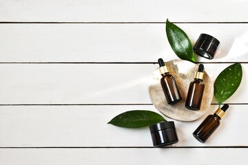 Brown bottles with pipettes and green leaves on a round wooden saw cut on a white wooden...