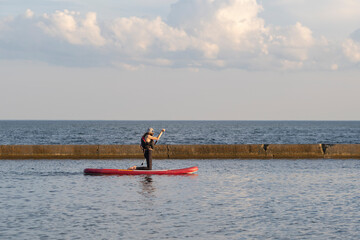 Young fit teenage girl in a life vest paddle boarding on a stand up board  at Lake Ontario. Summer activities and water sports. Space for copy. Selective focus.