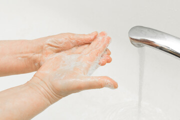 Fototapeta premium Elderly woman washes her hands with soap under the tap in the bathroom, the recommendation of frequent hand washing. Domestic hygiene