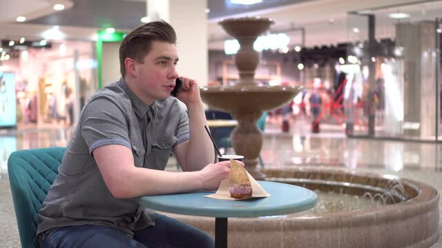 A young man in a cafe speaks on the phone against the background of a fountain. Decoration in the cafe.