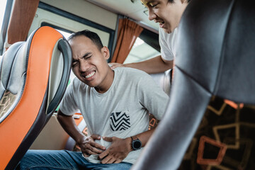 a man with a stomachache and his friend helped while sitting on a bus seat while traveling