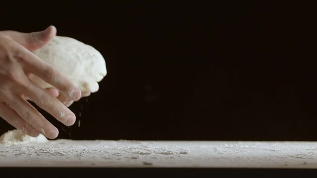 Male hands throw a piece of dough to a wooden table and sprinkle it with flour. Filmed on black background