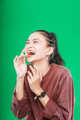 young Asian woman expressing wide-open mouth and raising hands in amazement isolated on green background