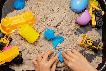 Child playing with kinetic sand and toy construction machinery. Hand of child in sand close up....