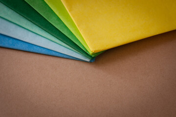 a stack of multi colored tissue paper spread out in a fan on a background of brown cardboard, with a vignette