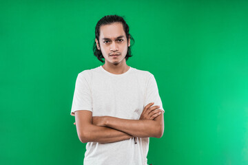 portrait of a handsome Asian man with a serious expression with his arms crossed, on a green...