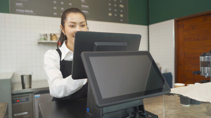 Asian woman barista people in apron working on POS system machine with blank empty space screen monitor on counter, cafe restaurant cashier. waitress in coffee shop. People lifestyle. Business service