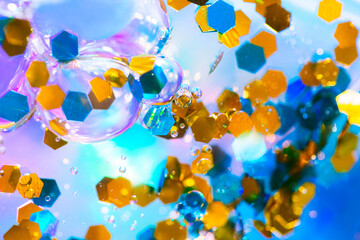 Fototapeta na wymiar Golden yellow and turquoise glitter in liquid with bubbles. Beautiful abstraction shot in close-up. Colorful macro texture