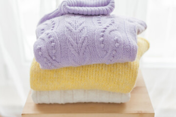 A stack of spring knitted clothes on a wooden chair. Yellow, Purple colors. Cozy.