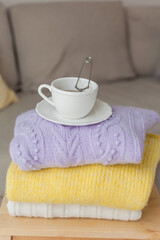 Fototapeta na wymiar A stack of spring knitted clothes on a wooden chair, a mug of hot tea with tea leaves. Yellow, Purple colors. Cozy.