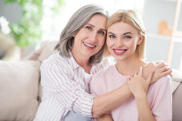 Fototapeta premium Portrait of two pretty cheerful ladies sit on sofa hugging hand on shoulder have good mood spend weekend indoors
