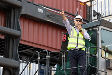 factory worker or engineer using walkie talkie for preparing a job beside truck in containers...