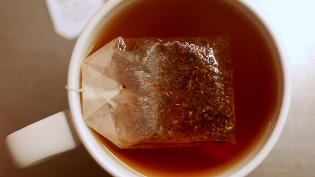 Making red caffeine free rooibos tea, tea bag in a white cup closeup